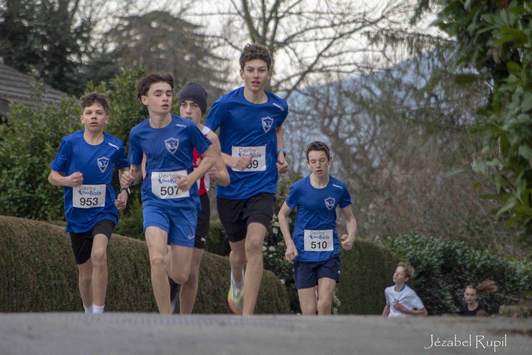 Young runners in blue club shirts tackling a climb at the Derby des Bois